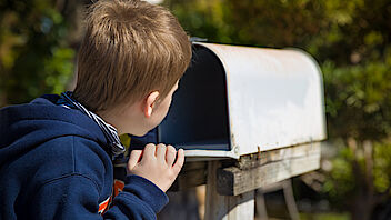 JPG: Junge schaut in leeren Briefkasten