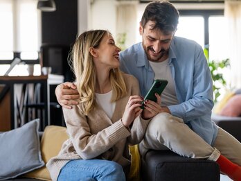 SWU Paar Lachend am Handy auf Sofa