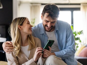 SWU Paar Lachend am Handy auf Sofa
